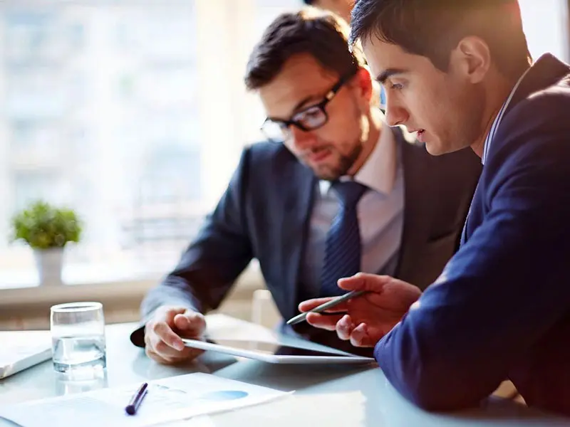 Two men sitting at a table looking at something on their phone.